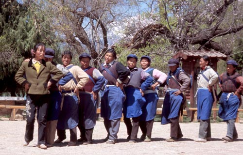 Naxi women sport a blue apron, backpack, and cap.